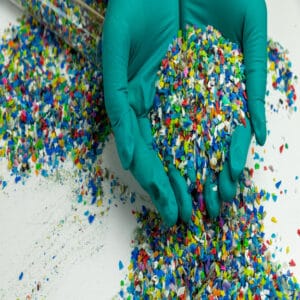 Crushed plastic on green gloved hand. Reuse of plastic. polymer beads. Scraps obtained from plastic waste. The world's plastic reduction policy. Scraps plastic on white background.
