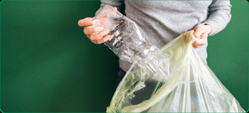 Un hombre coloca una botella de plástico aplastada en una bolsa reutilizable, mostrando prácticas responsables de reciclaje y reduciendo los residuos de plástico de un solo uso.
