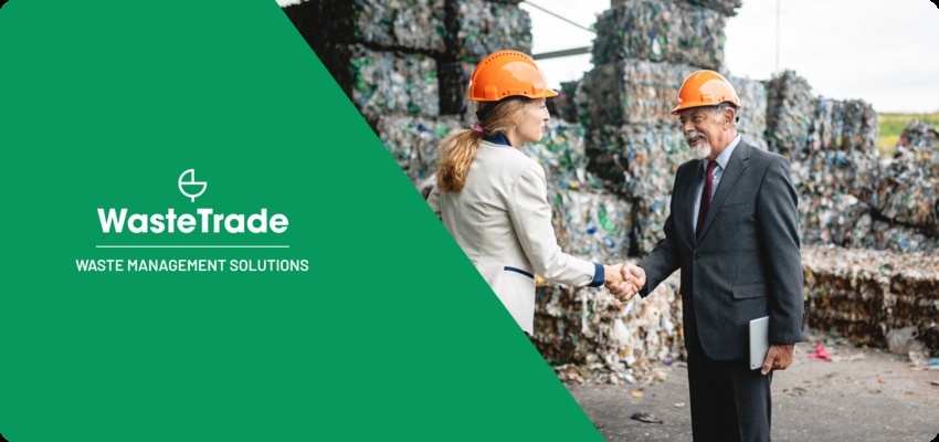 Business professionals in safety helmets shaking hands in front of a pile of compacted recyclables, representing waste management collaboration.